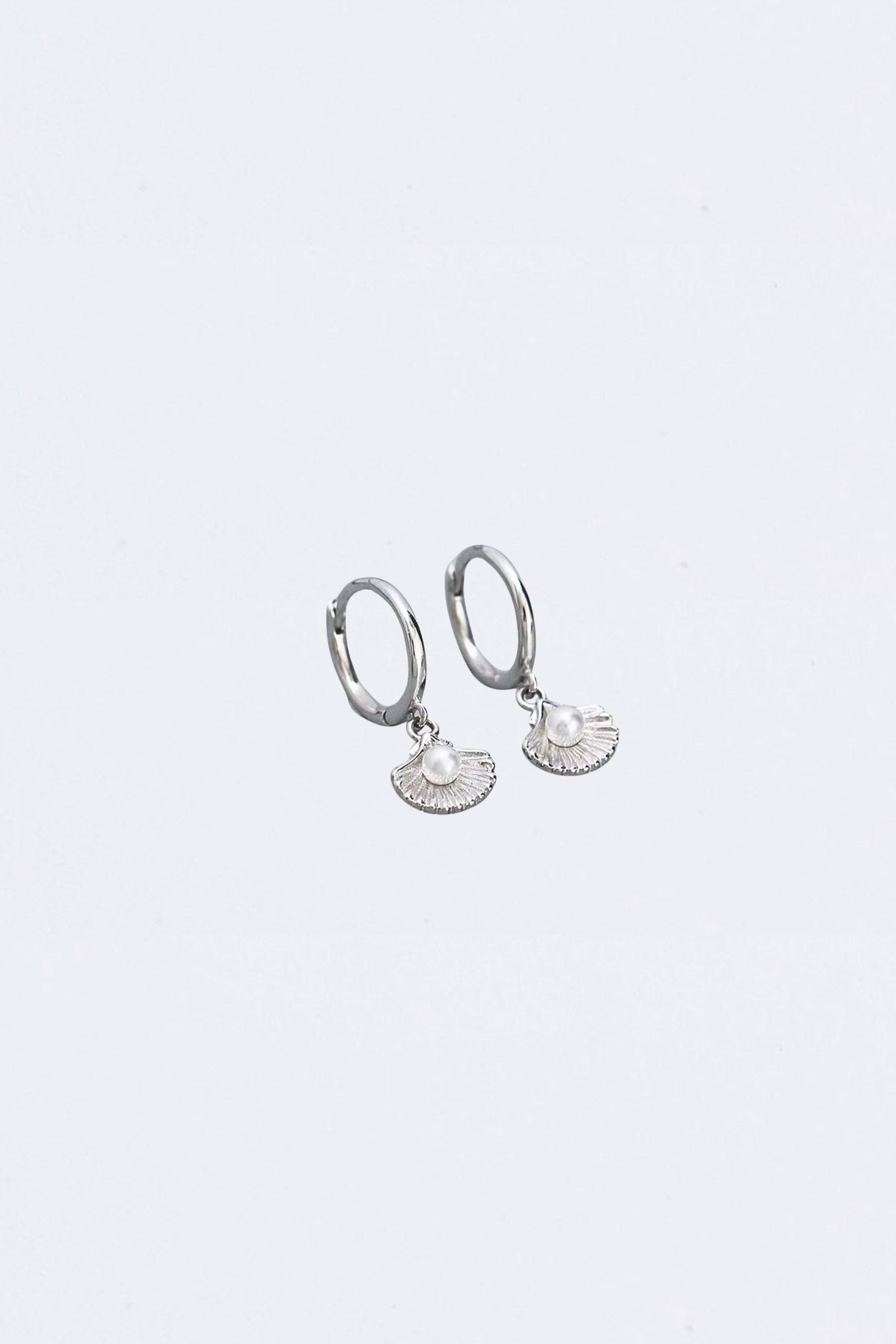 Silver hoop earrings with clam shell and pearl charms on a light gray background