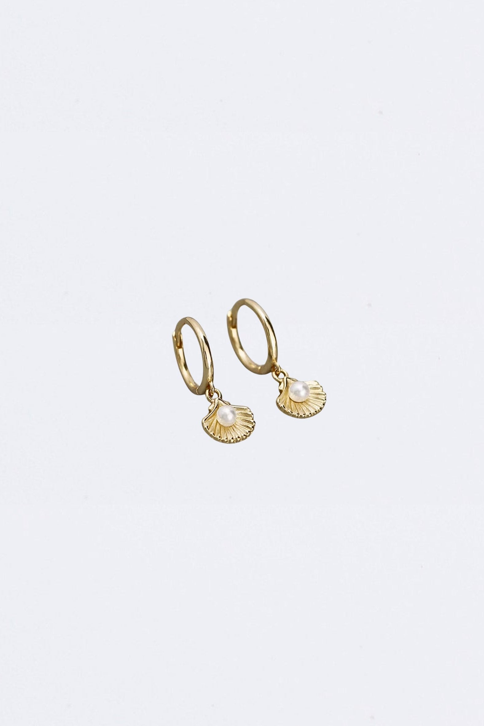 Gold hoop earrings with clam shell and pearl charms on a white background