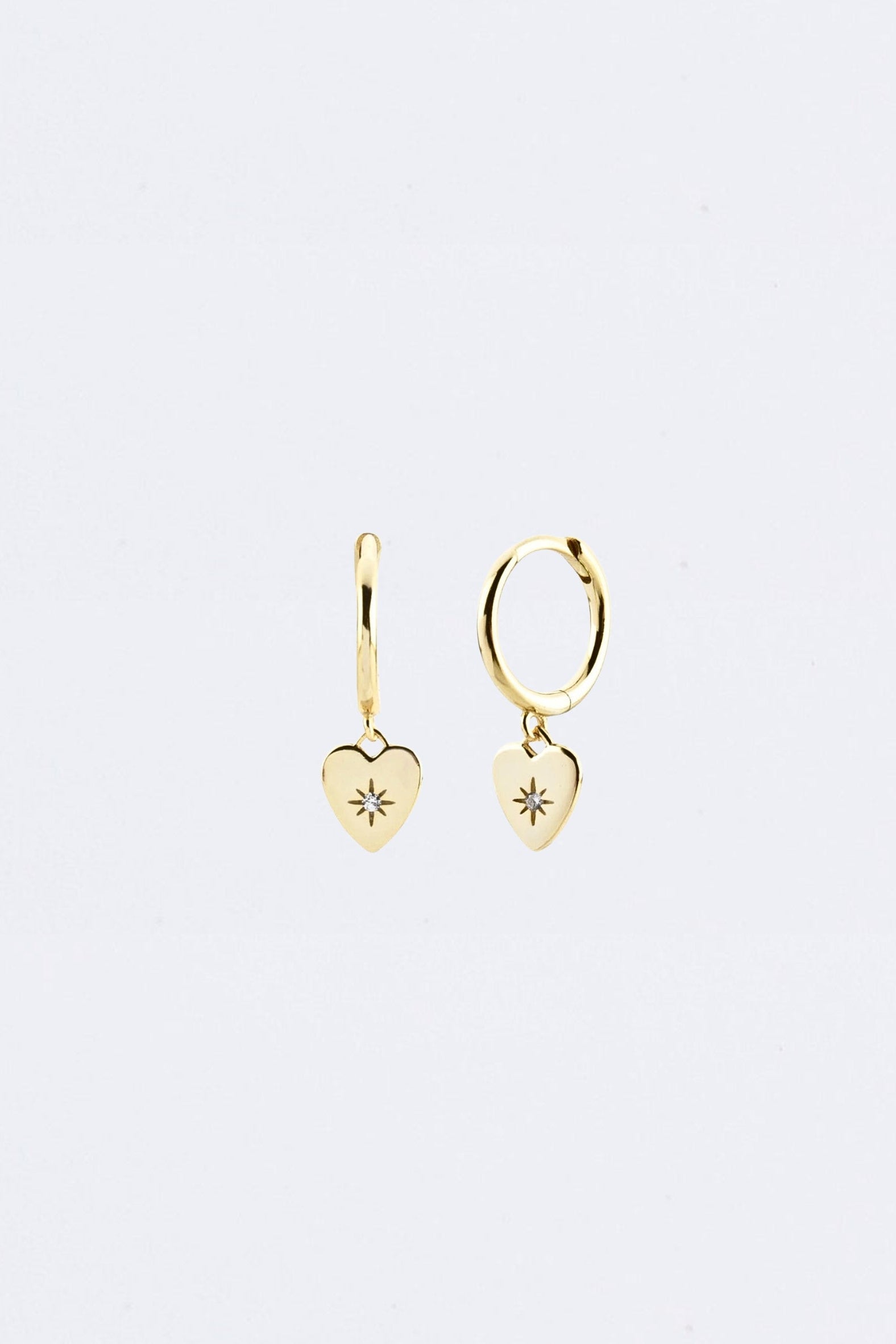 Gold heart-shaped earrings on a light gray background Maraux Love Heart Huggies Maraux Jewellery