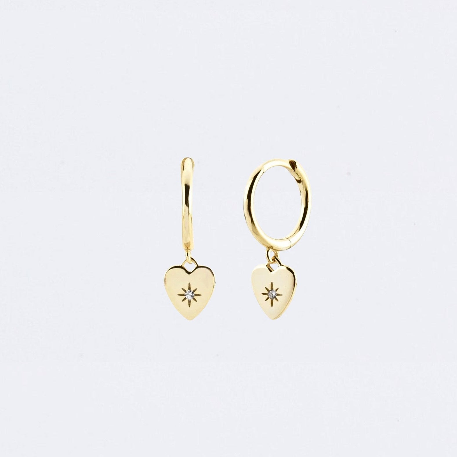 Gold heart-shaped earrings on a light gray background Maraux Love Heart Huggies Maraux Jewellery