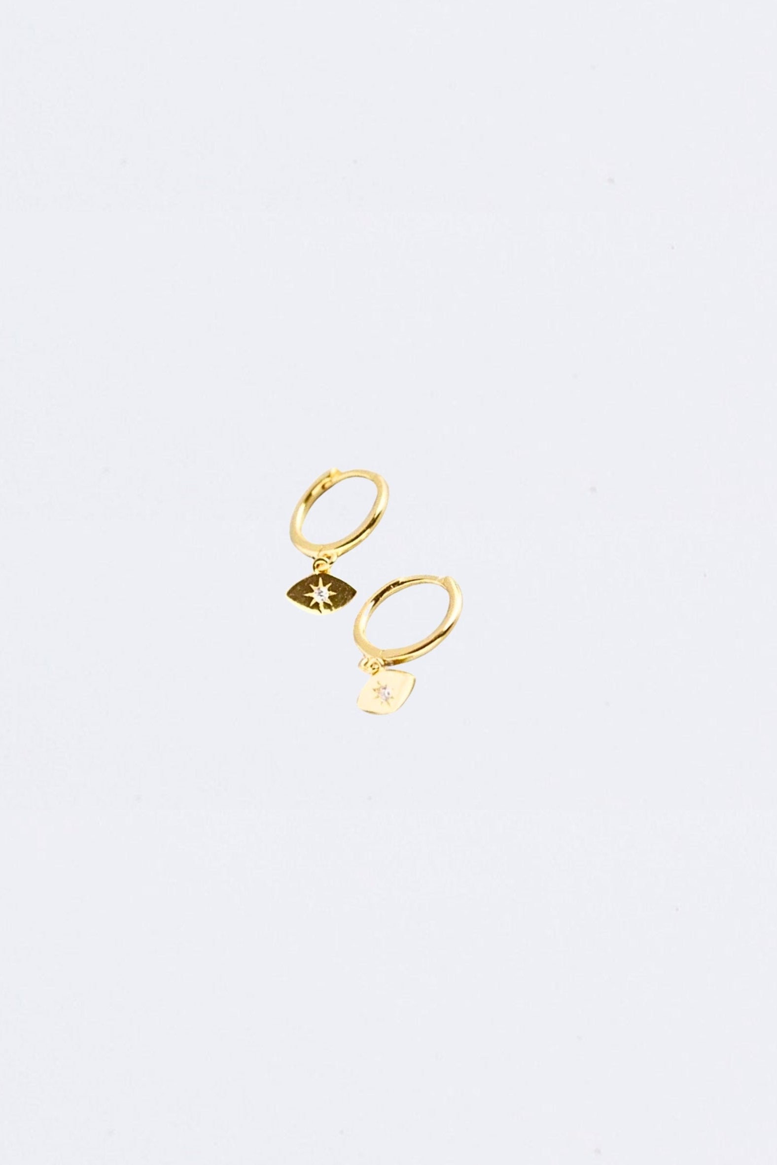 Gold evil eye huggie earring with star detail on a light gray background