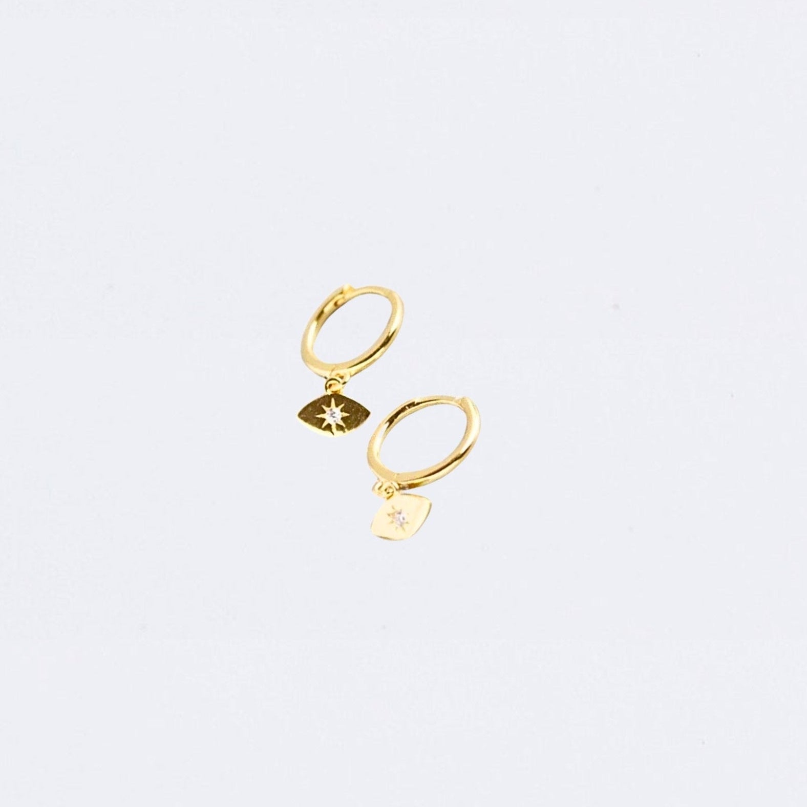 Gold evil eye huggie earring with star detail on a light gray background