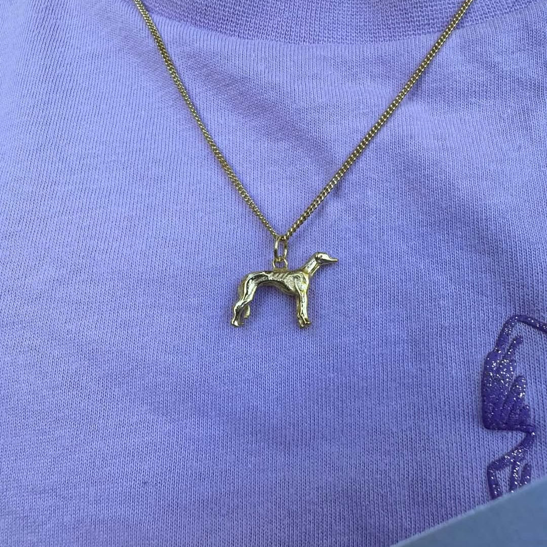 Greyhound dog-shaped pendant on a chain against a purple shirt background