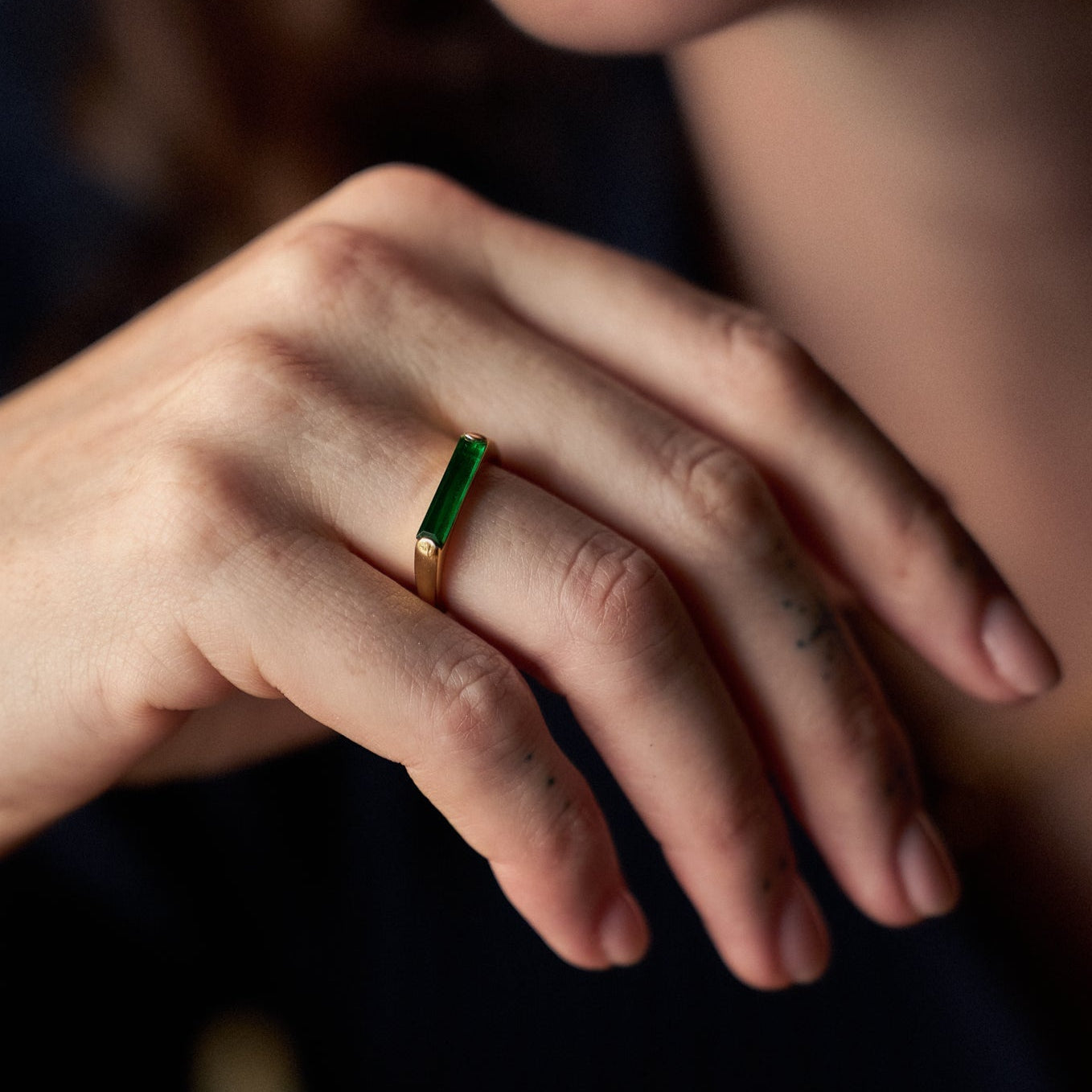 Close-up of a hand wearing a green gemstone ring with a blurred background