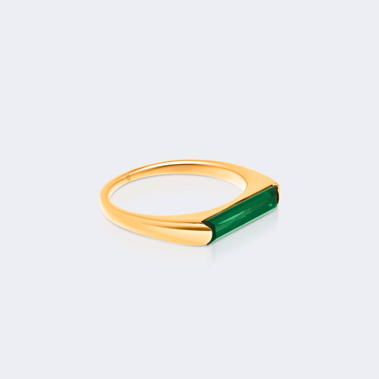 Gold ring with a green gemstone on a light gray background