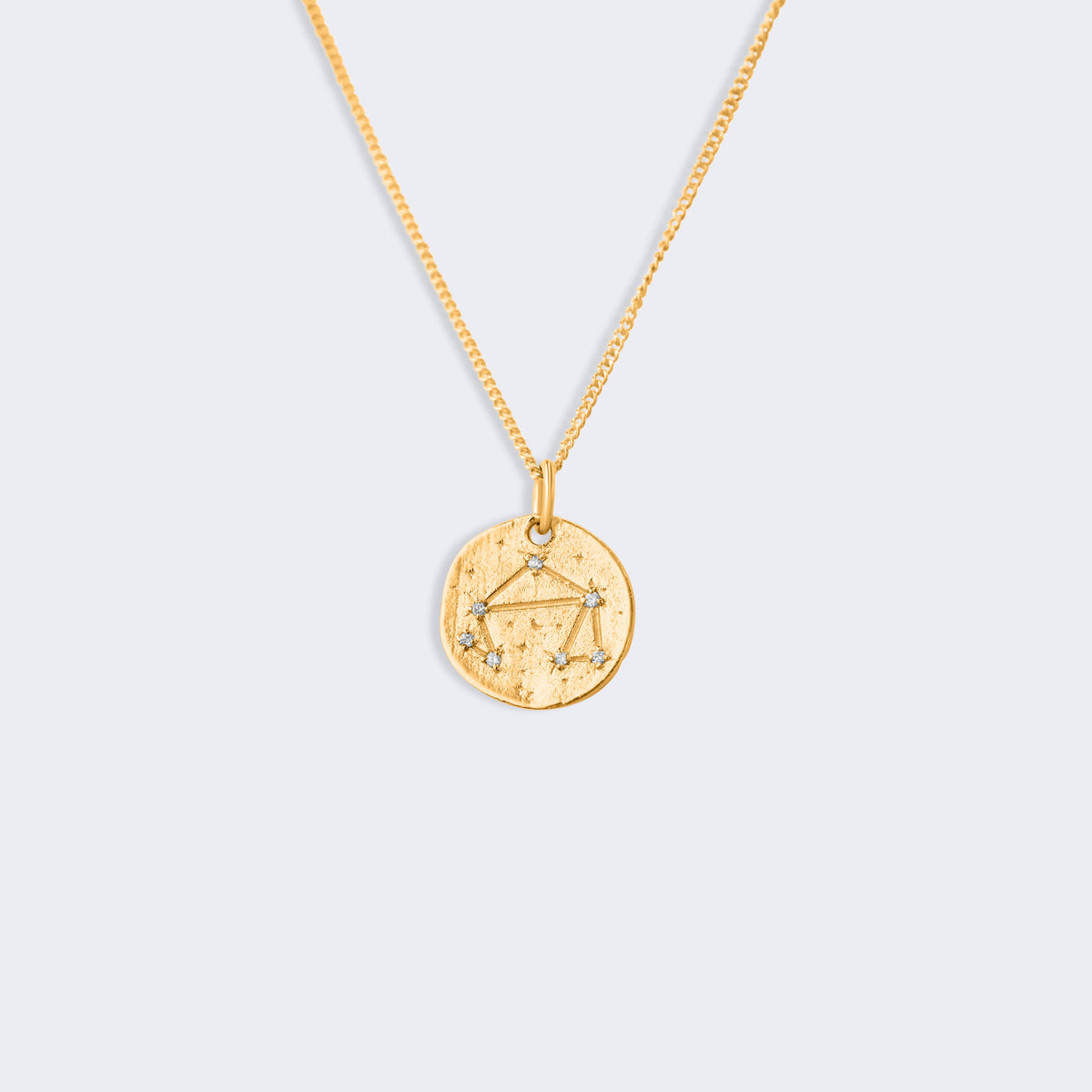 A gold chain necklace with a round, textured gold pendant featuring a star and constellation design for libra