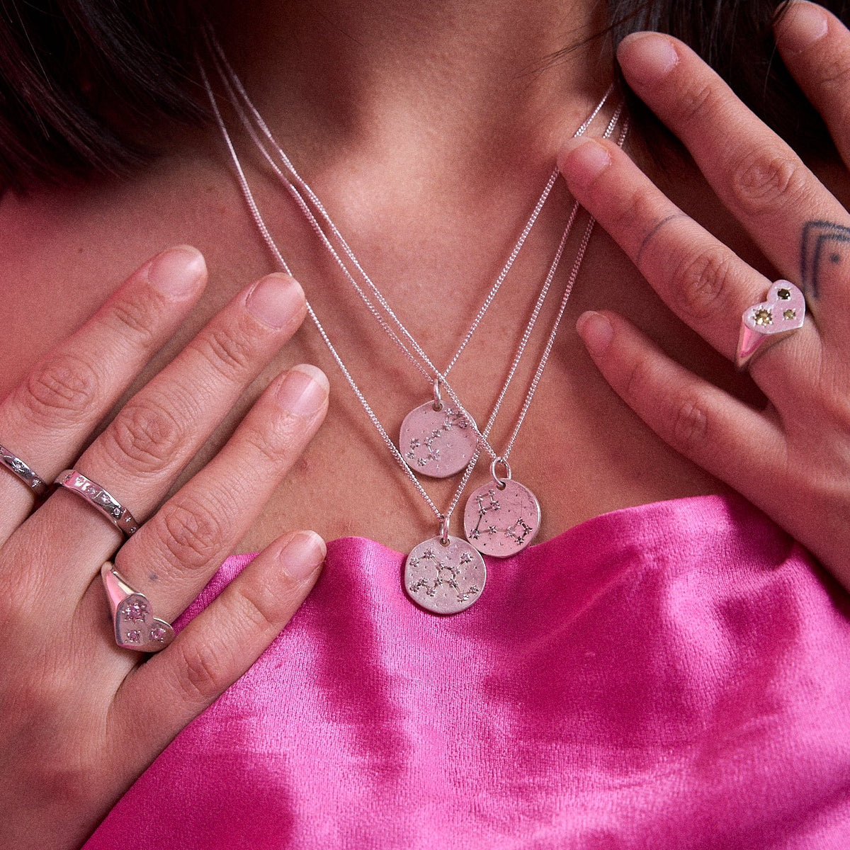 Model wearing layered sterling silver Maraux zodiac constellation necklaces with star signet rings
