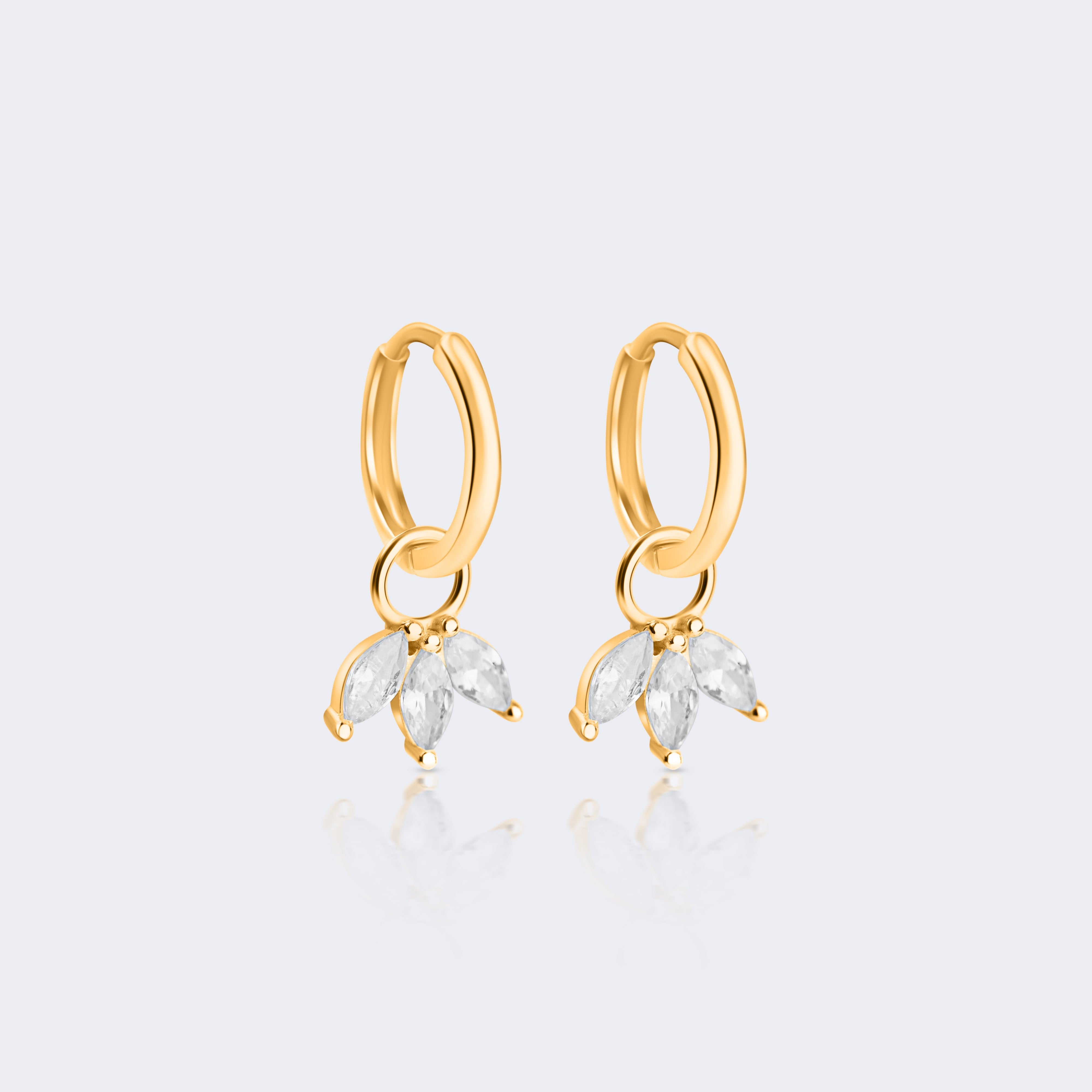 A pair of gold huggie hoop earrings with dangling marquise-cut clear crystals, shown on a light gray background with a soft reflection below.