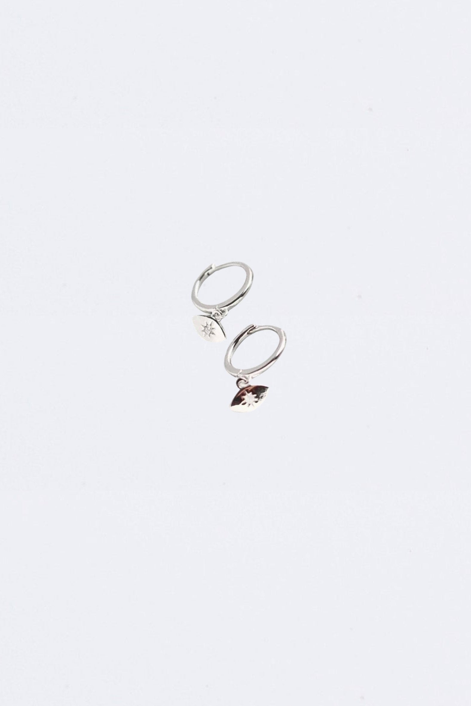Silver hoop  evil eye huggie earrings with a small  charm on a light gray background