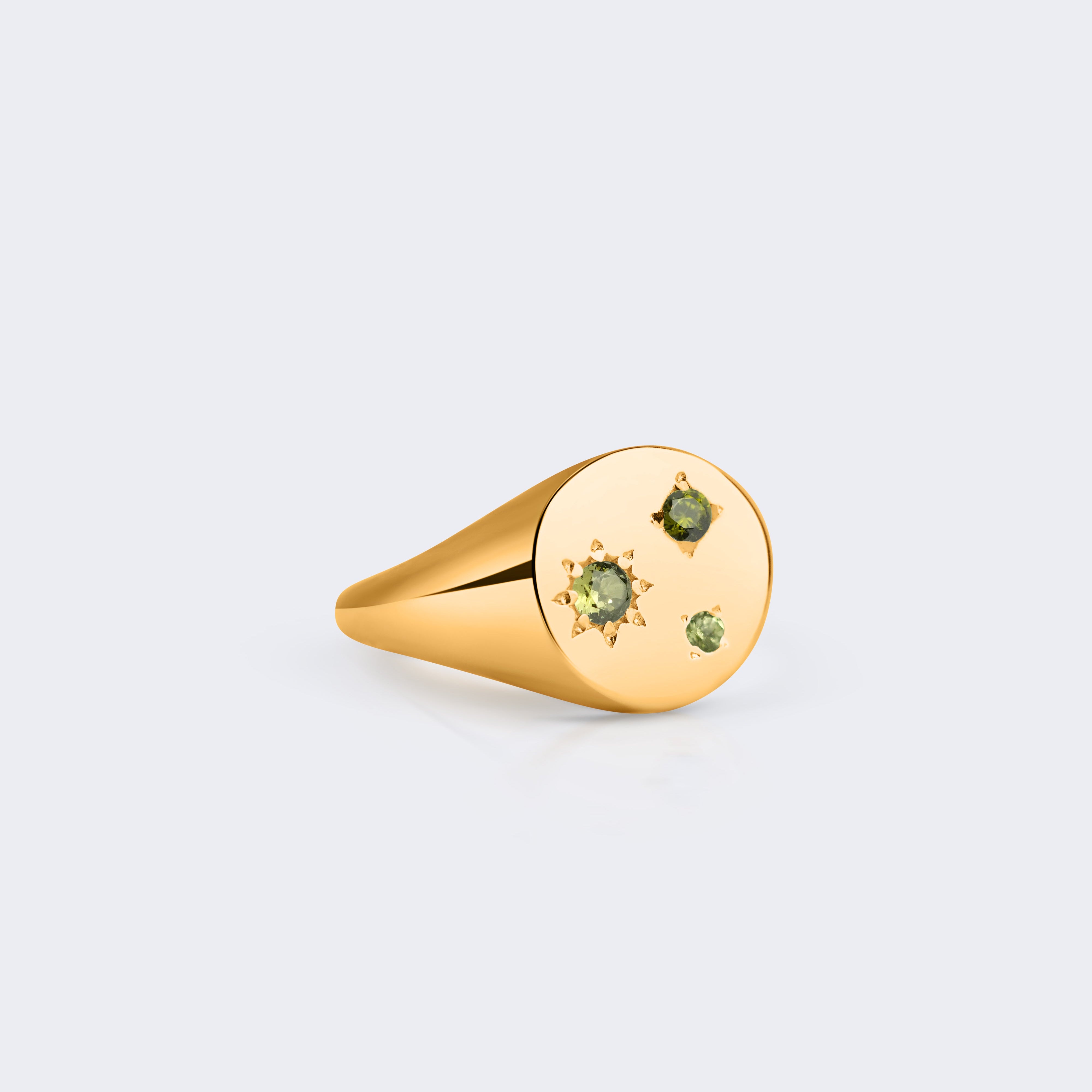 A gold signet ring with three small green gemstones set on its oval face