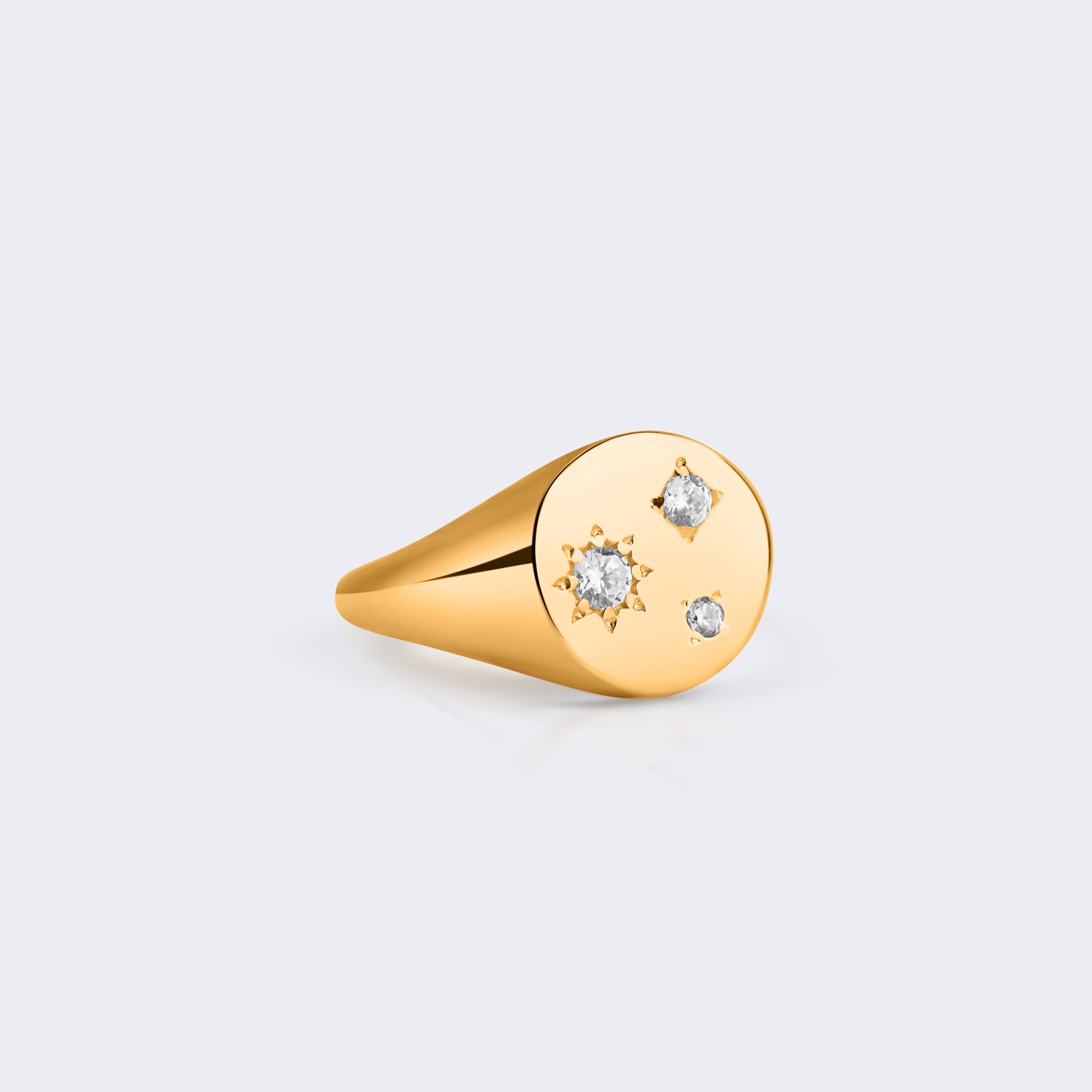 A gold signet ring with a flat oval face featuring three small clear gemstones