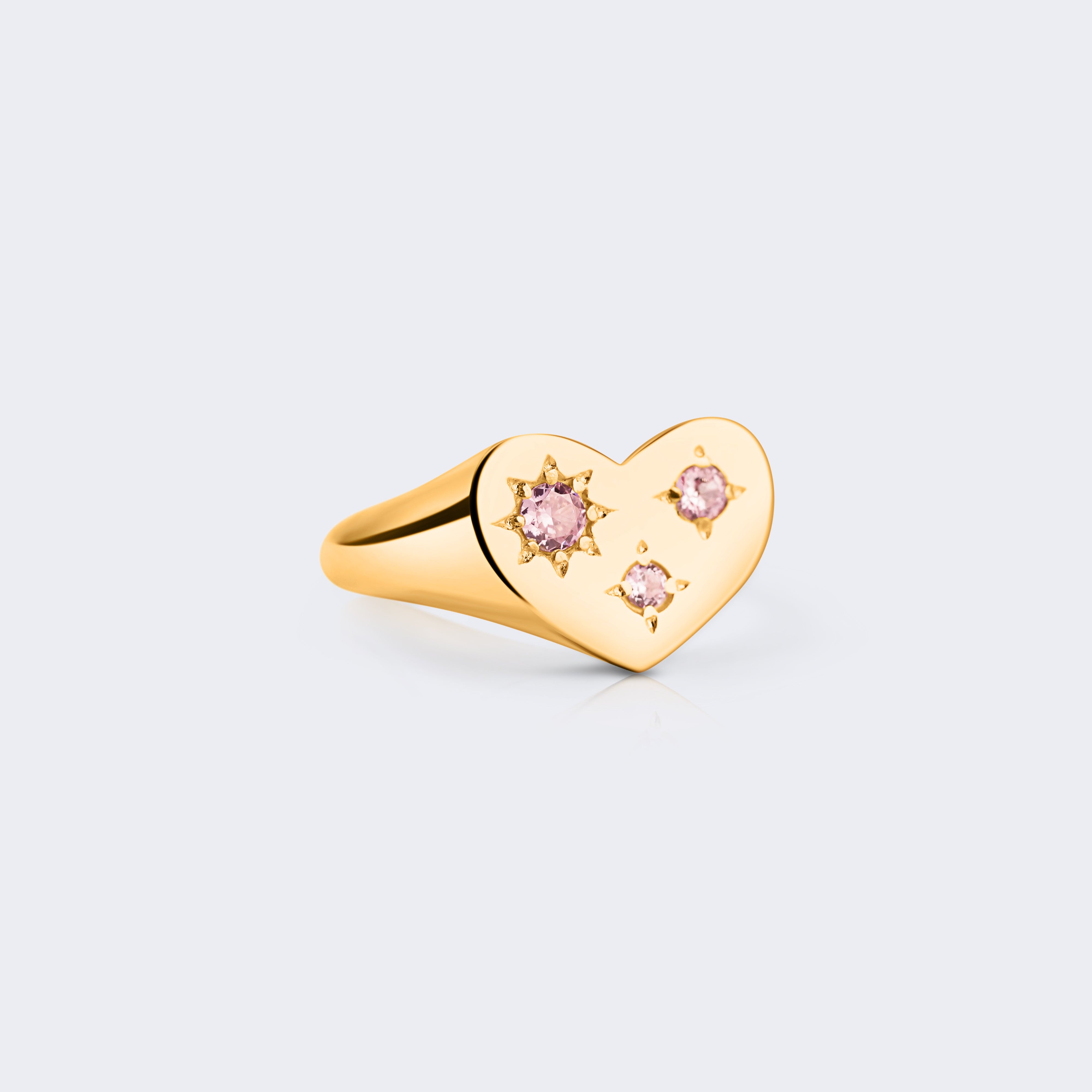 A gold heart-shaped signet ring with three small pink gemstones
