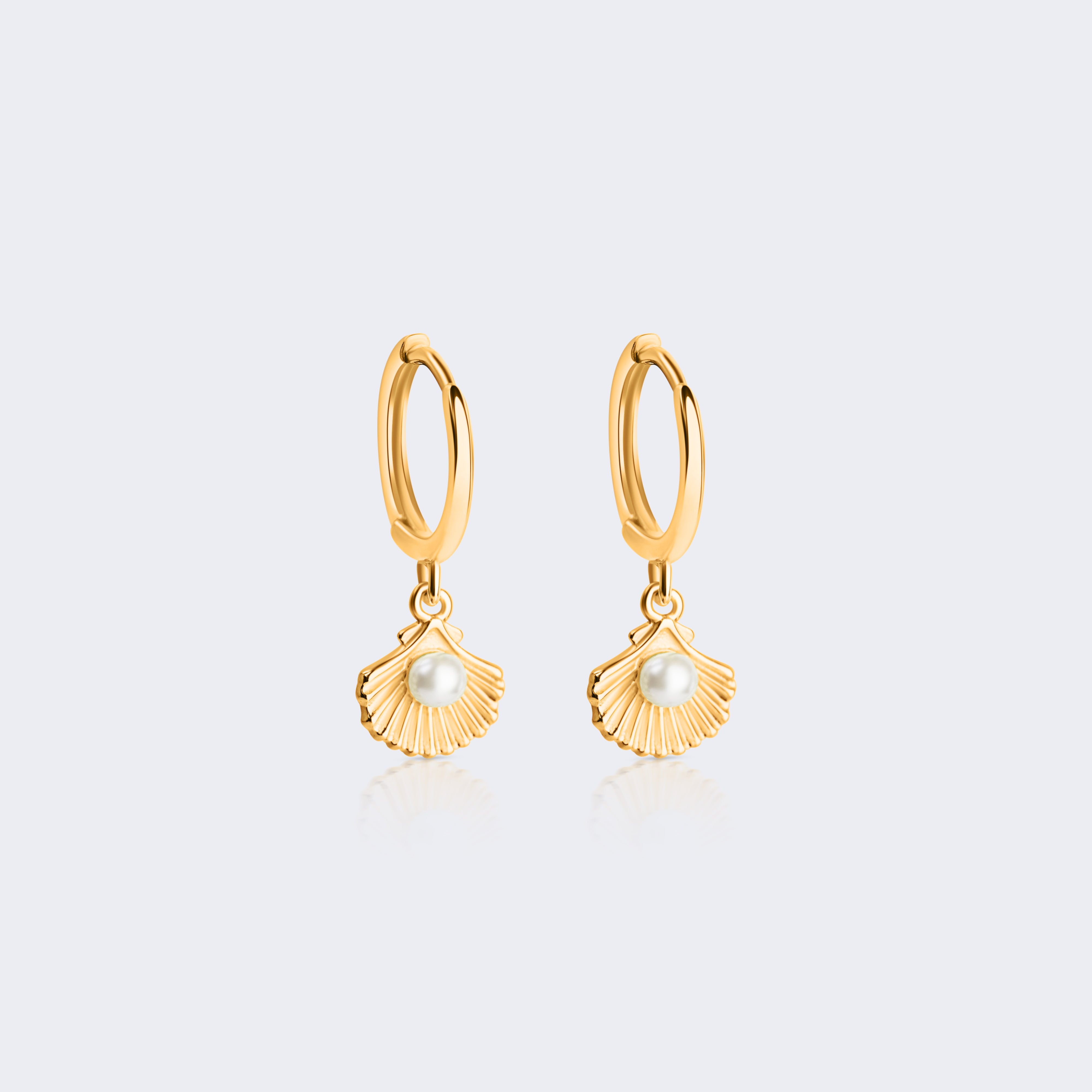 A pair of gold huggie hoop earrings with dangling textured shell charms, each accented with a small white pearl, shown on a light gray background.