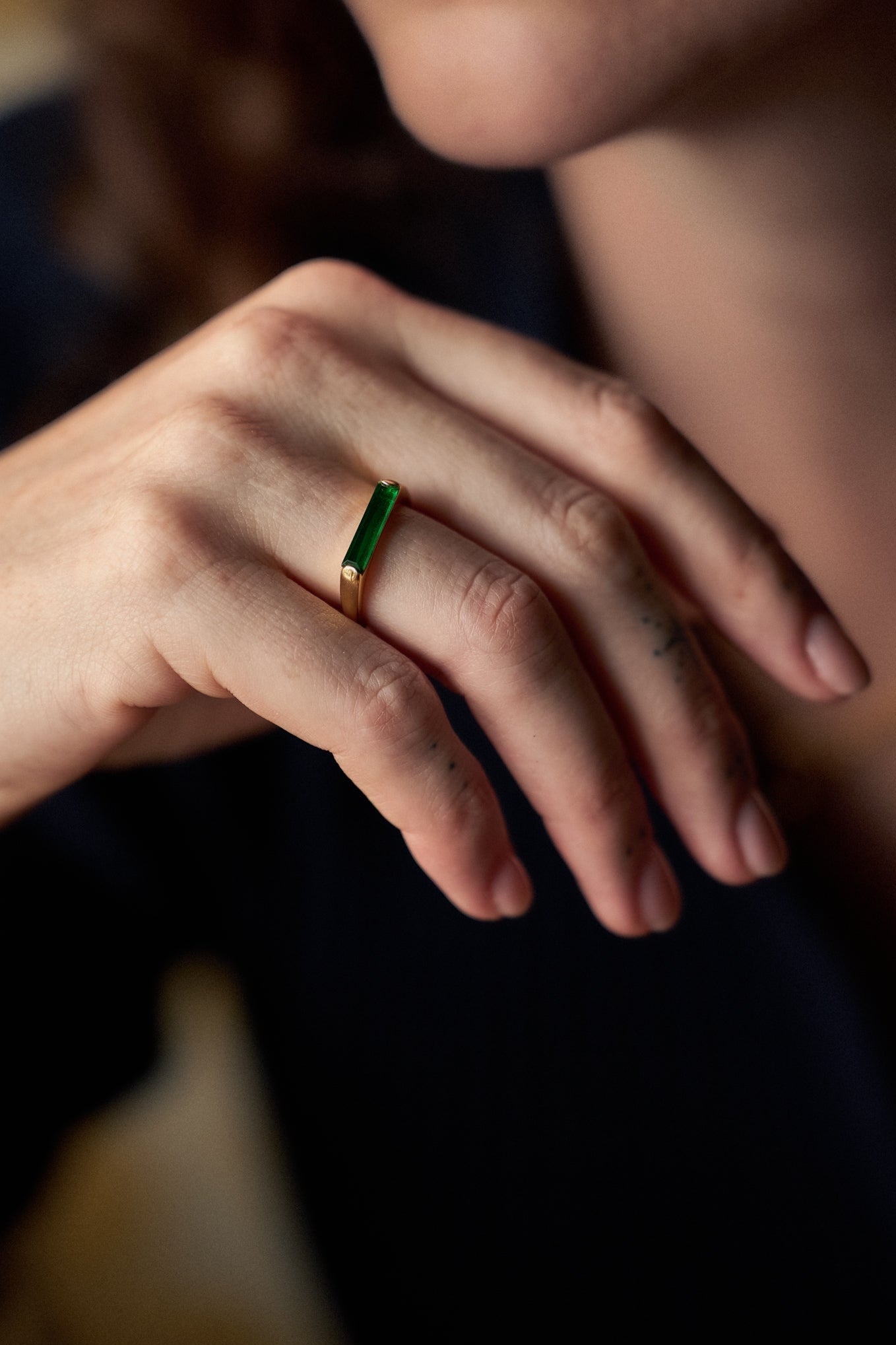 Close-up of a hand wearing a green gemstone ring with a blurred background