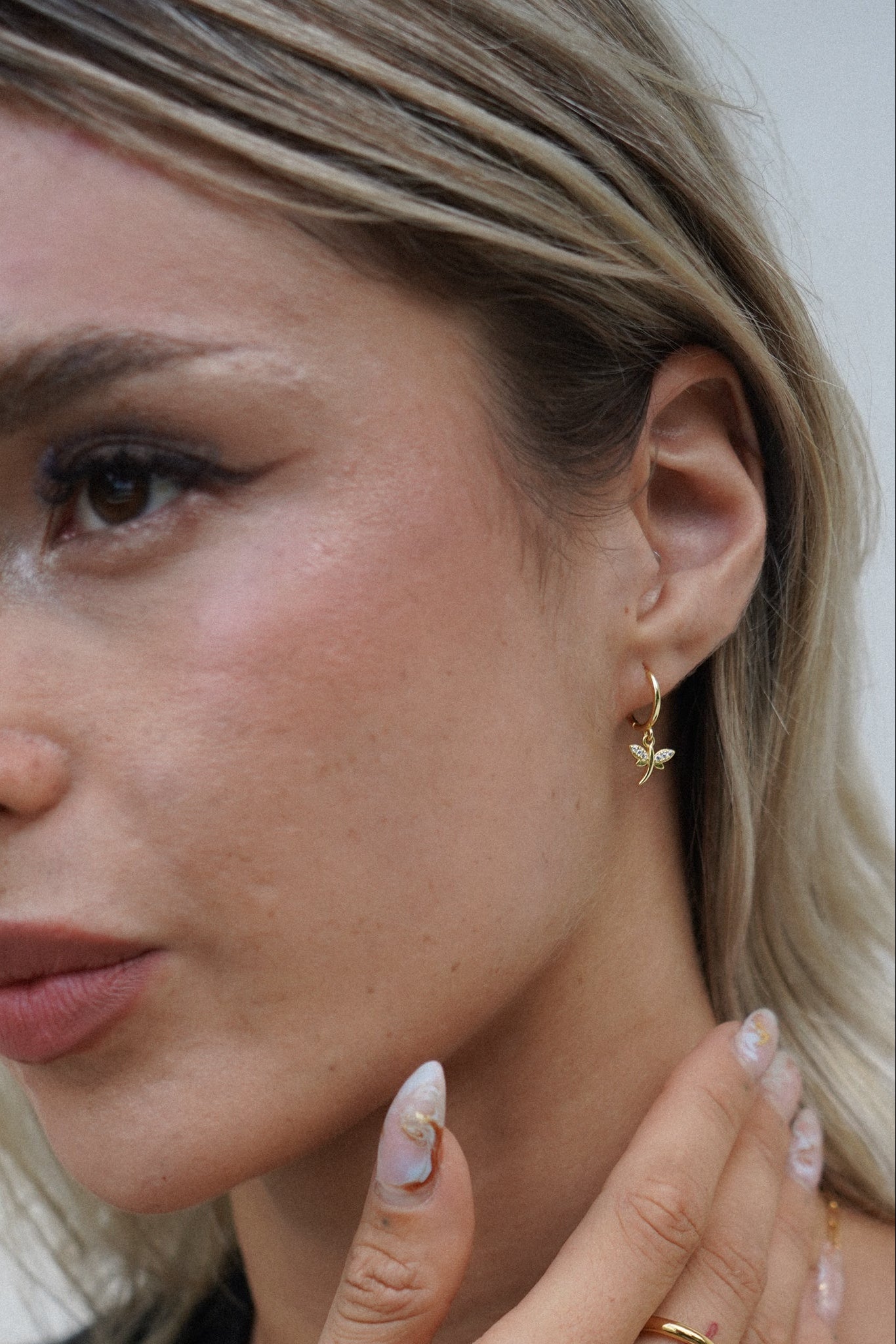 Close-up of a woman wearing small gold huggie earrings with a dragonfly charm on them