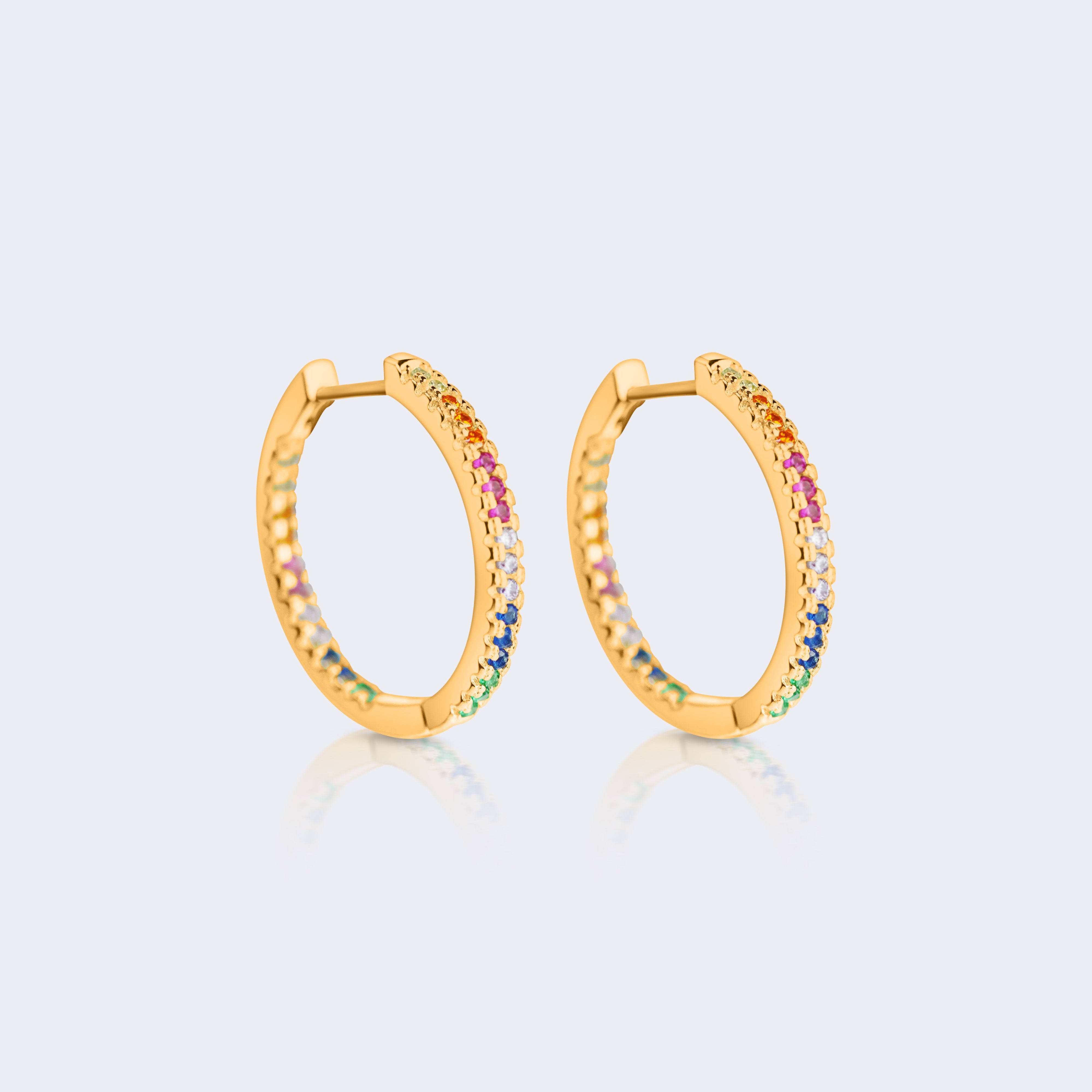 A pair of gold hoop earrings with small rainbow-colored gemstones set along the lower half, displayed on a light gray background with a soft reflection.