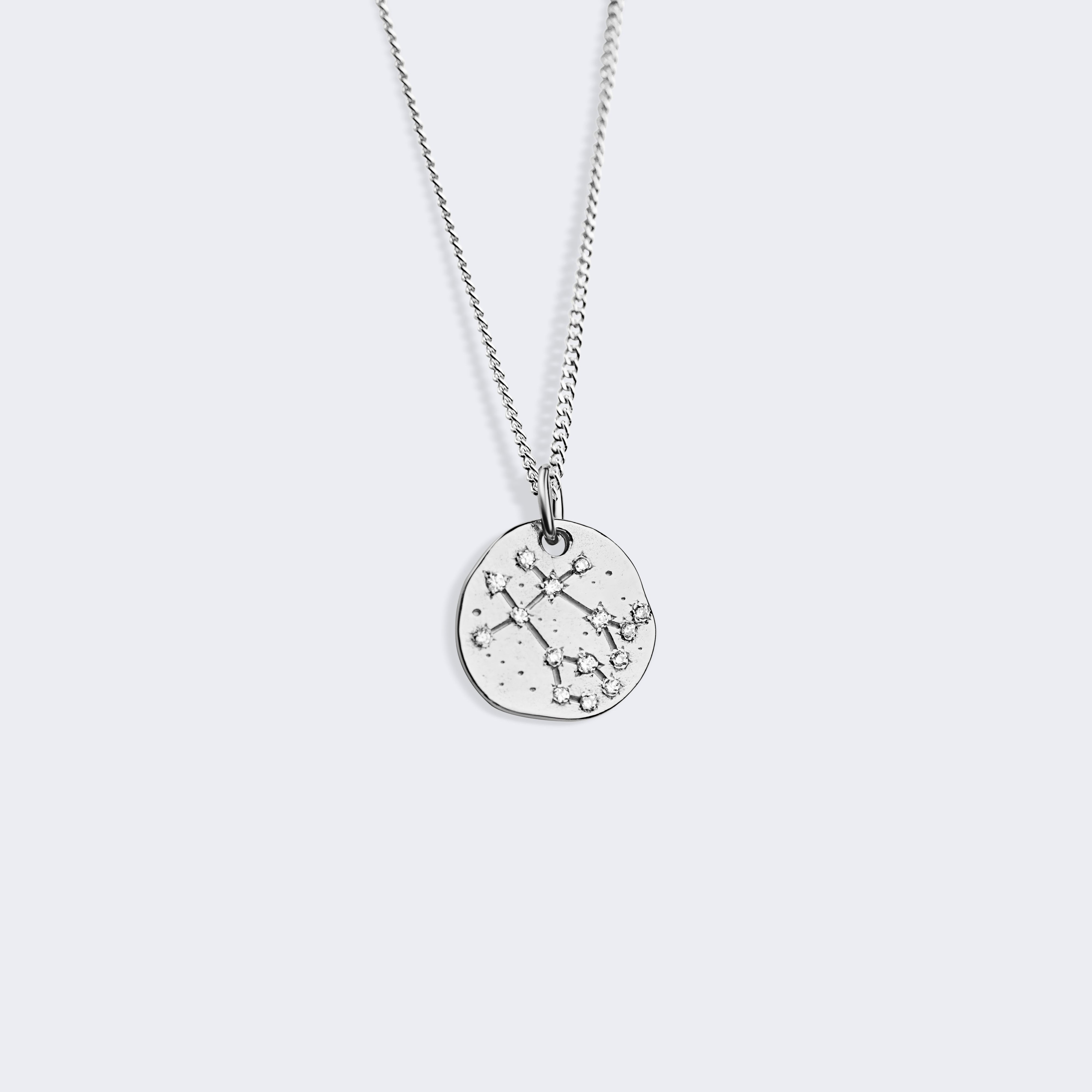 A silver chain necklace with a round, textured silver pendant featuring an gemini star constellation with small sparkling zircons as stars